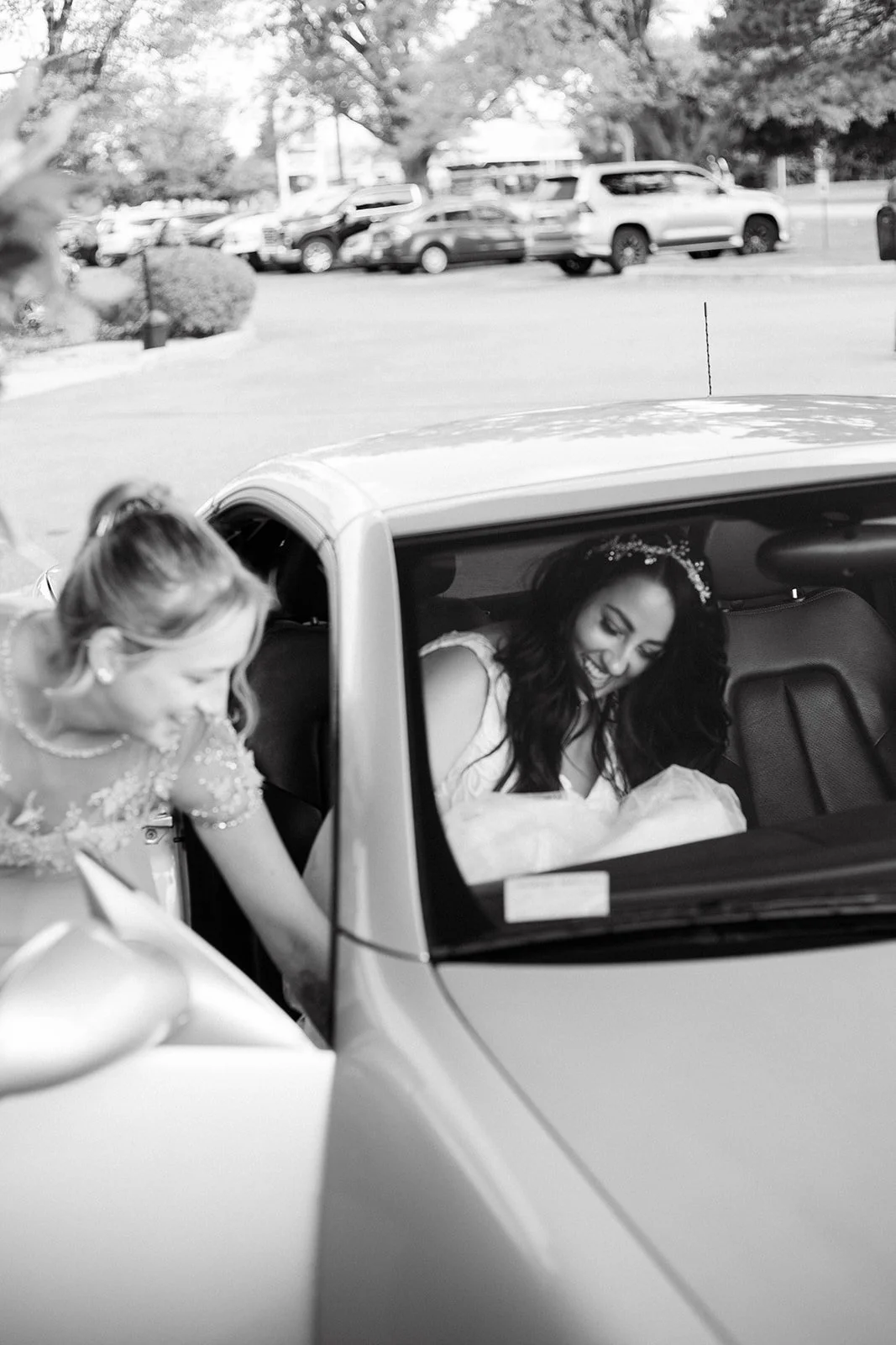 A bride sitting inside a car with a big smile, while a woman leaning into the car, talking to her, also smiling. At Glenhyrst Gardens in Brantford, Ontario.