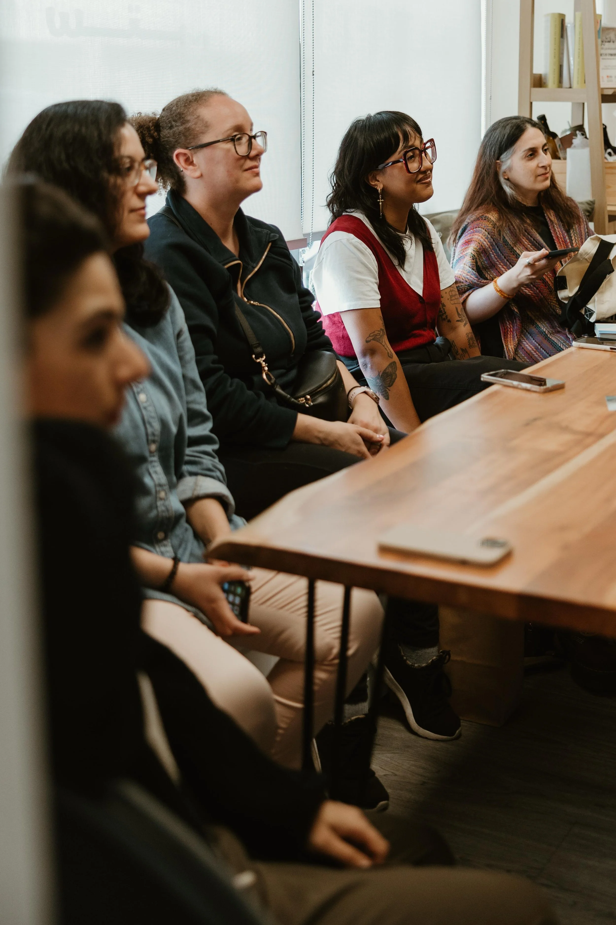 A group of women sitting at a long wooden table in an indoor setting, listening attentively, with some holding phones or notepads, at Sitti Hub in Mississauga, Ontario.