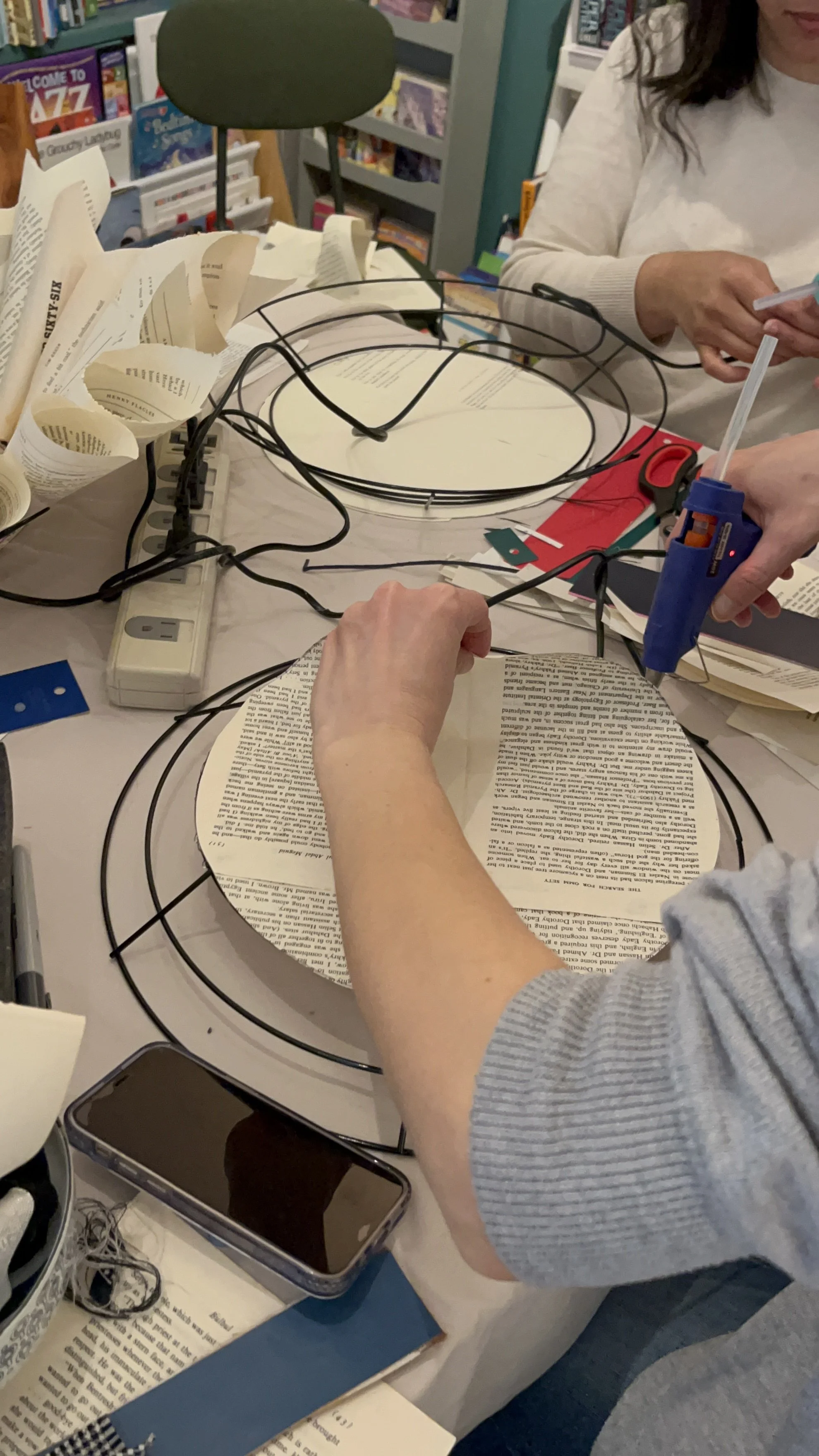 participants making book page wreaths at Slow Craft Co. craft class workshop in Nashua NH arm holding hot glue gun to glue paper to wreath frame for crafting