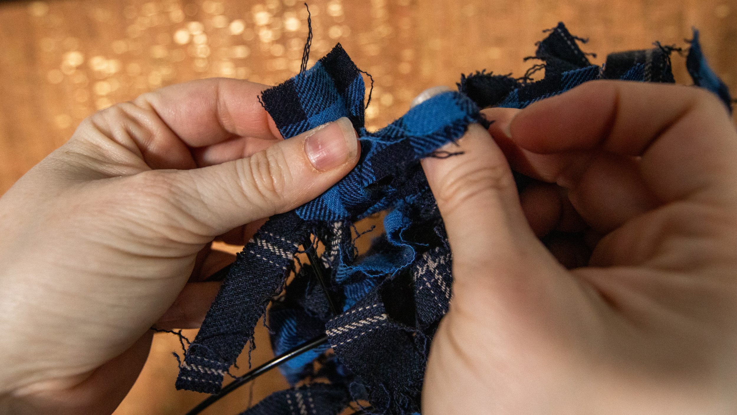 close up hands tying blue plaid fabric to wire wreath frame in front of sparkly cork background