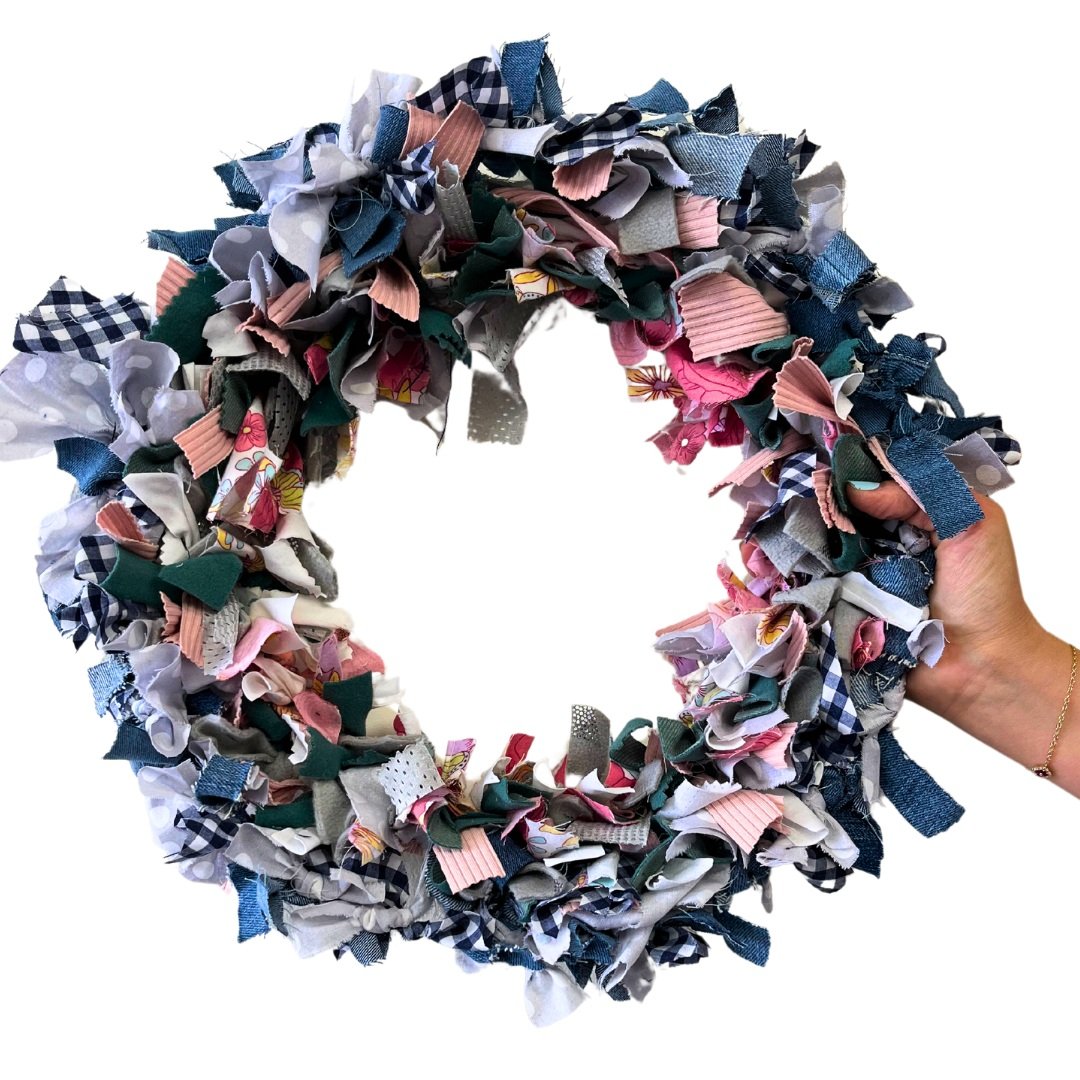 upcycled wreath using repuposed materials in spring colors denim and gingham with a hand holding the wreath from the side