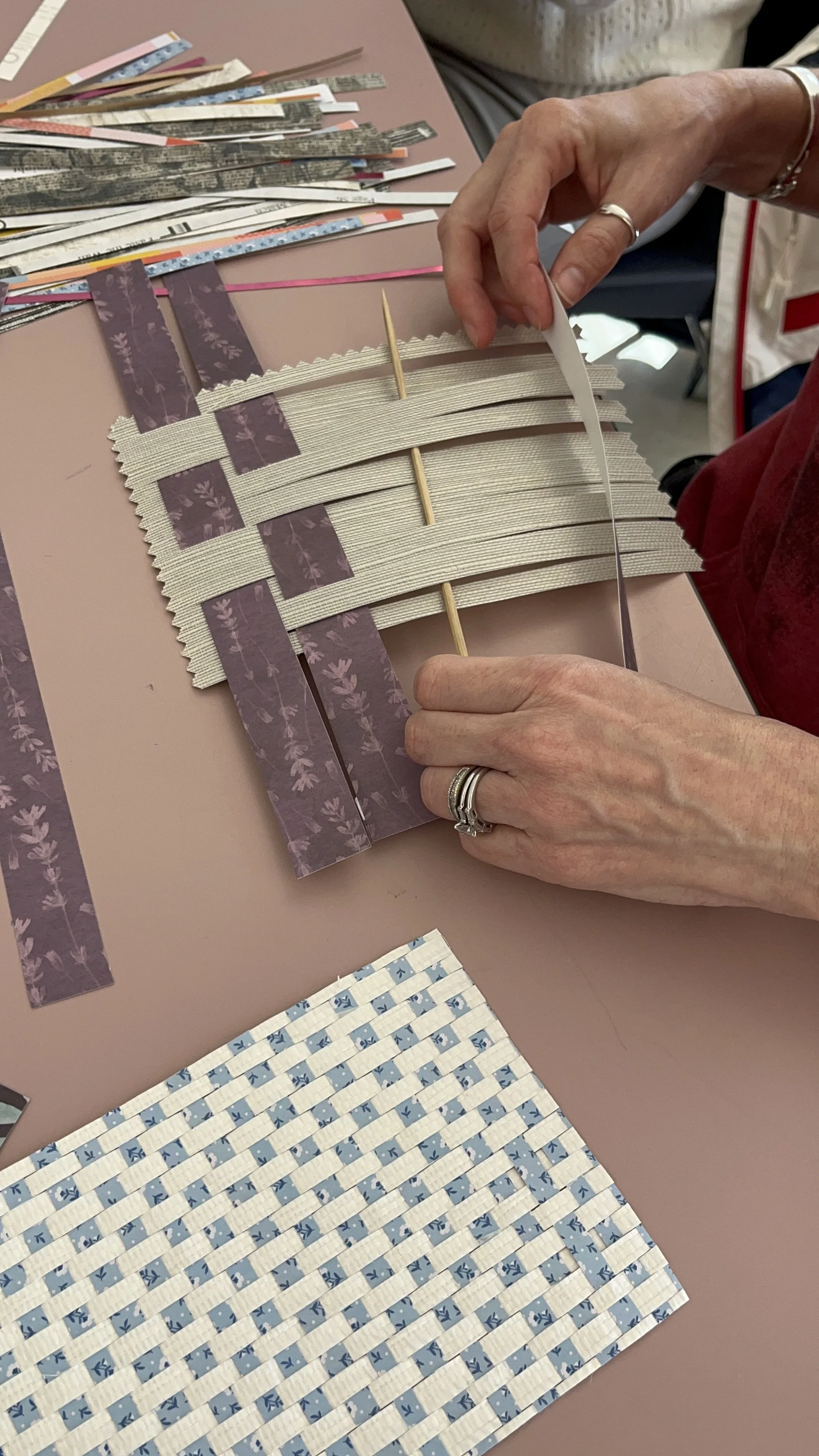 hands weaving paper in purple and cream, close up image at the table looking down