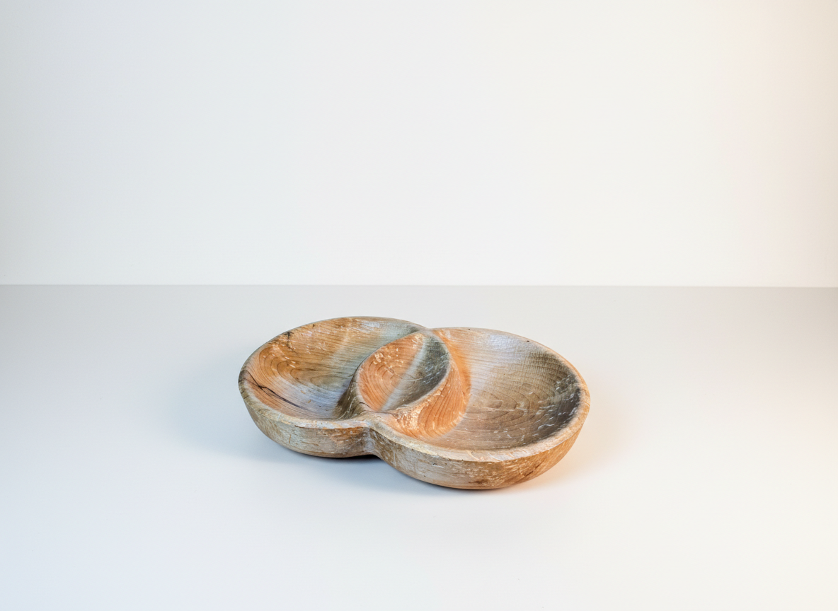 A wooden bowl with two compartments, placed on a white surface against a white background.