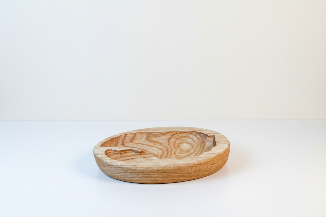 A round wooden bowl with carved patterns on a white surface with a plain wall background.