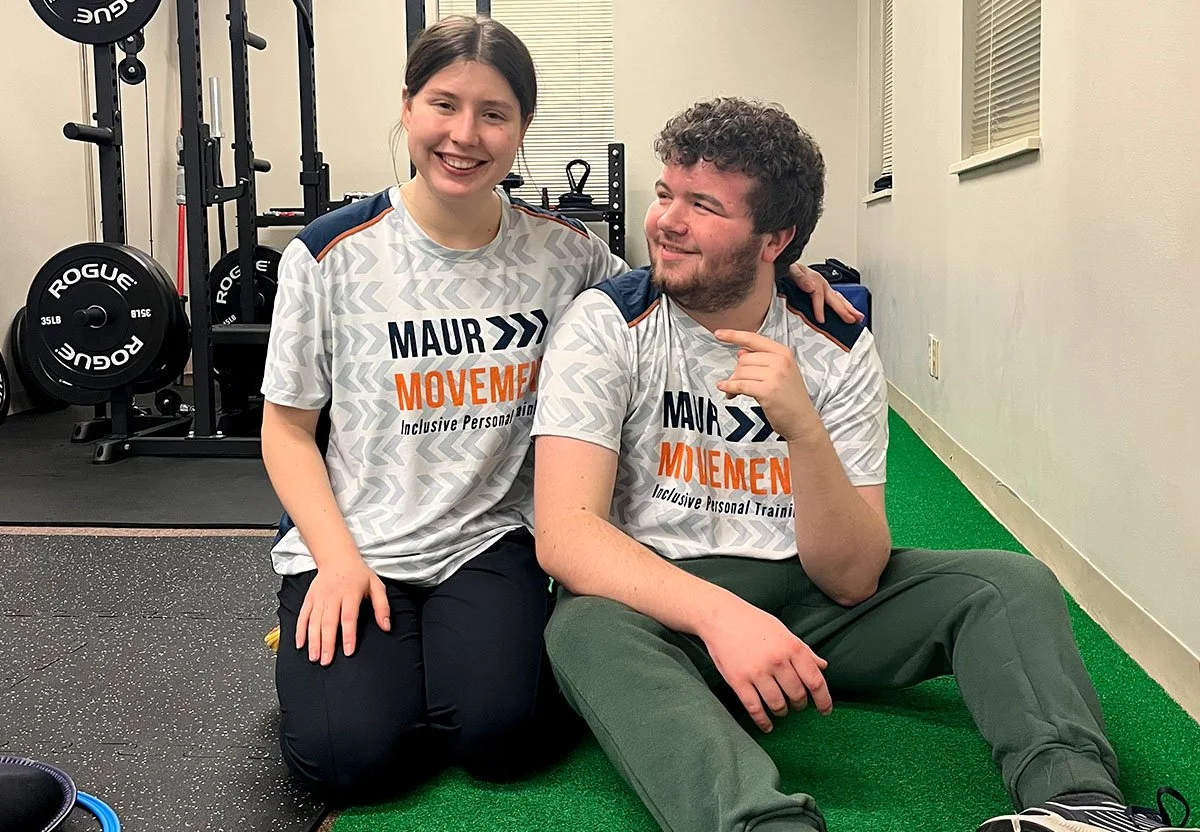 Adaptive trainer and student sitting on green turf in gym