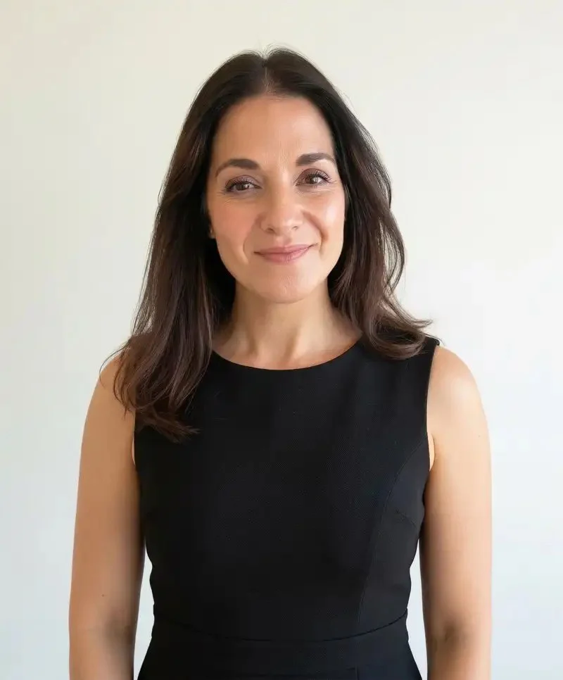Angi Milano, Founder & CEO of Maven Advisory with shoulder-length dark brown hair wearing a sleeveless black dress, standing against a plain off-white background.