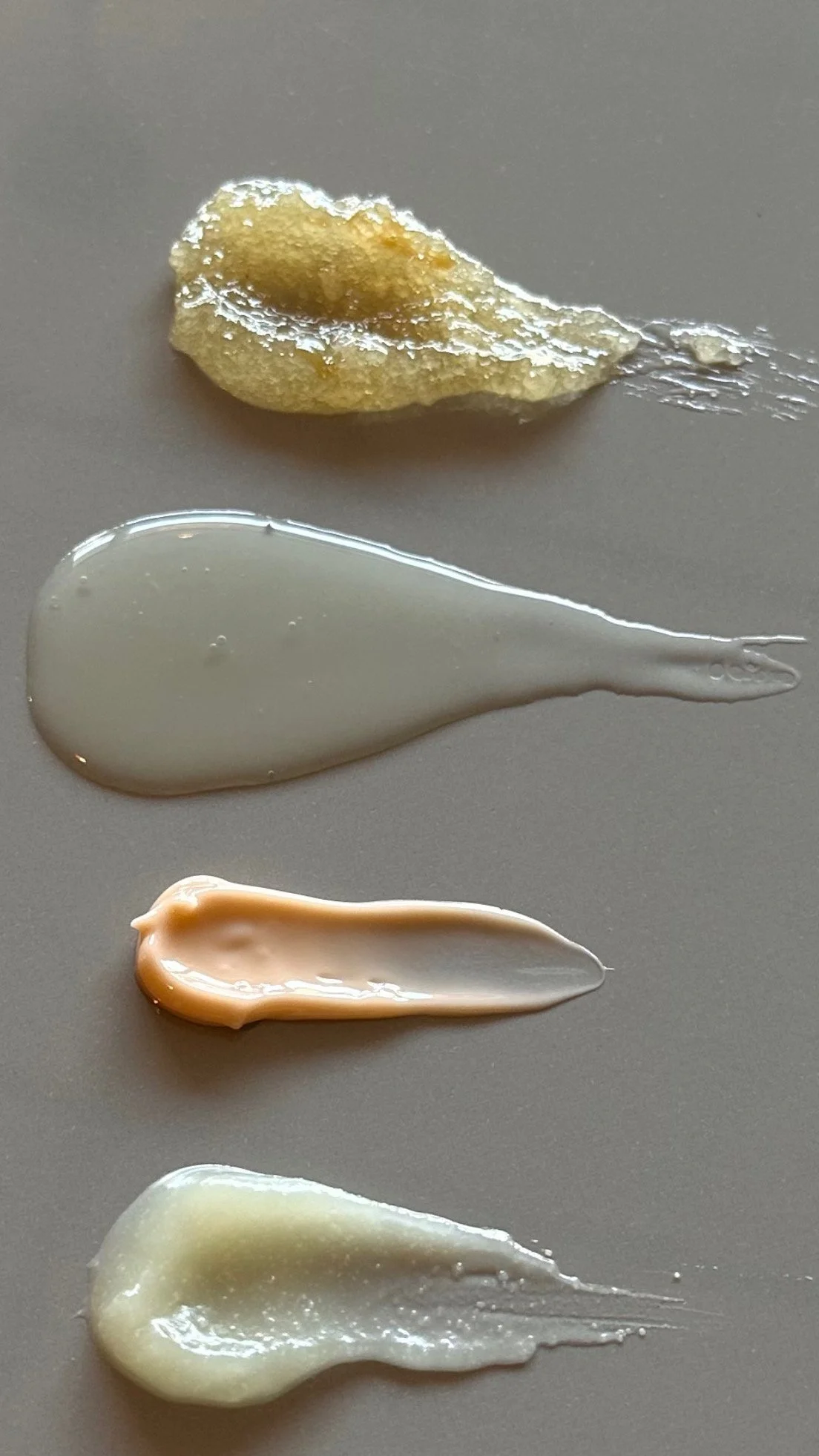 Four different shades and textures of cream or lotion samples applied in streaks on a flat surface.