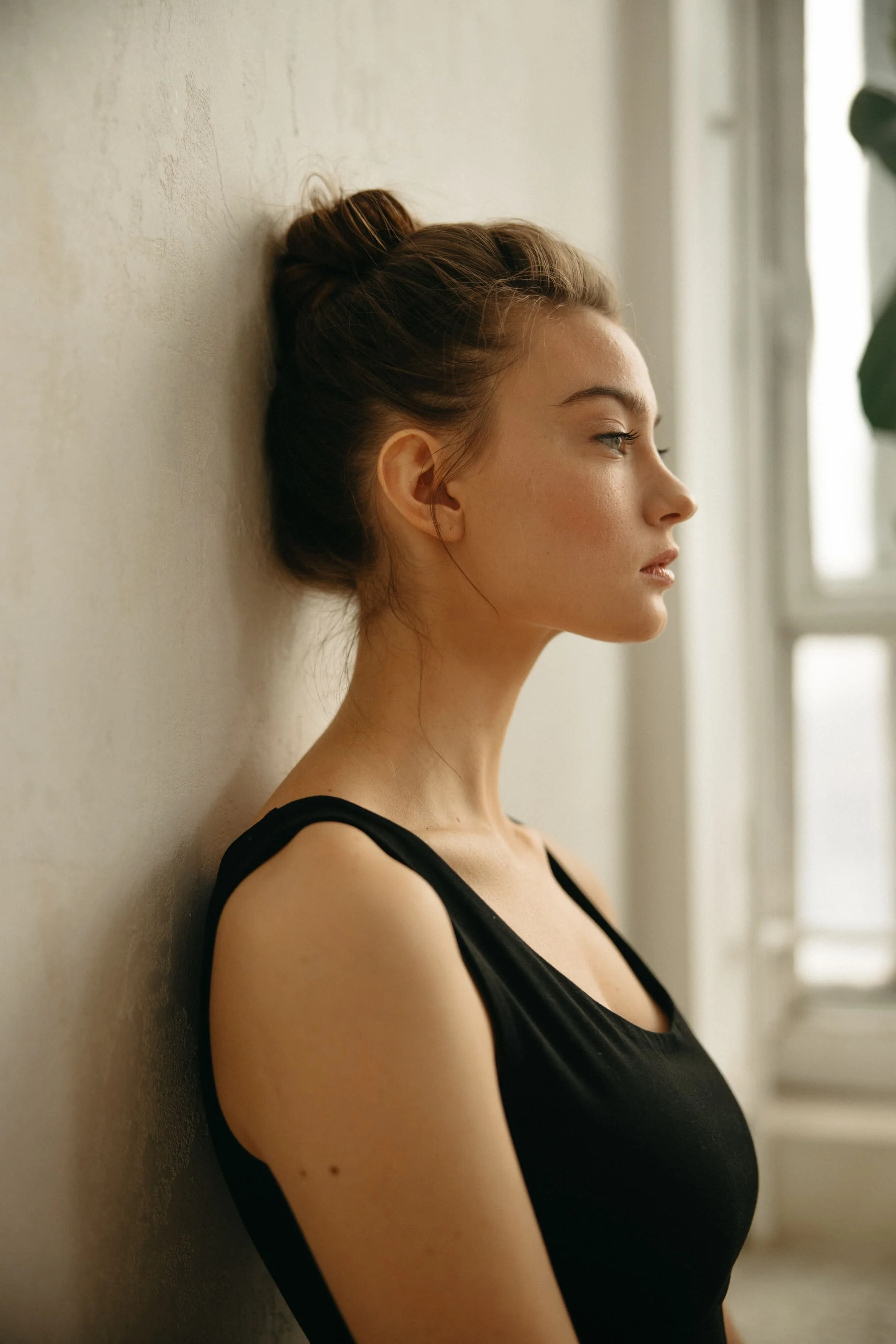 Side profile of a woman in a black tank top by a window, illustrating how breast reduction scars stay hidden under everyday necklines in Denver