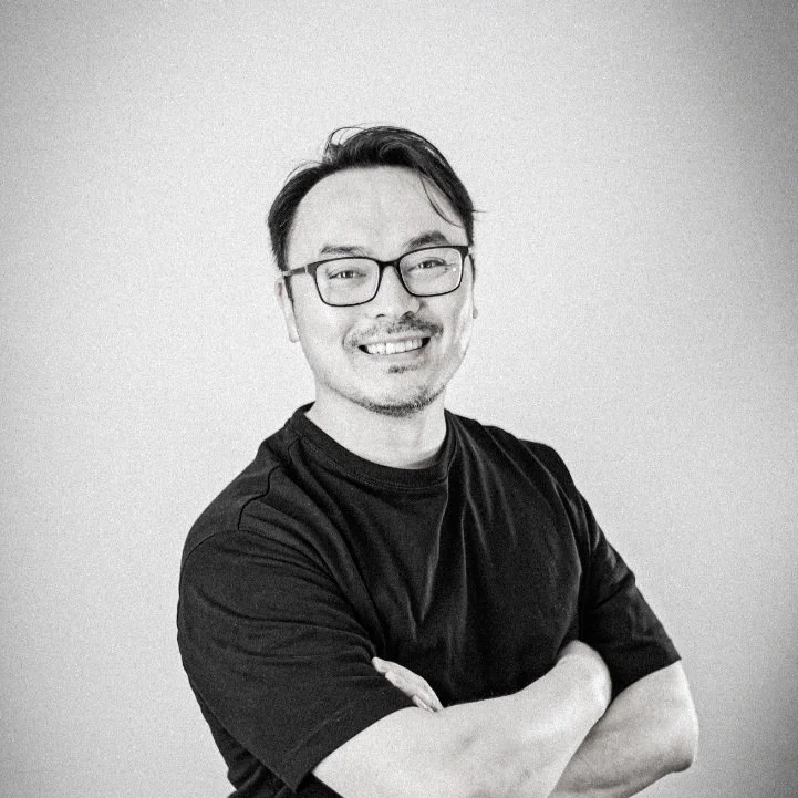 Man with glasses smiling, wearing a black t-shirt, arms crossed, against a plain background.