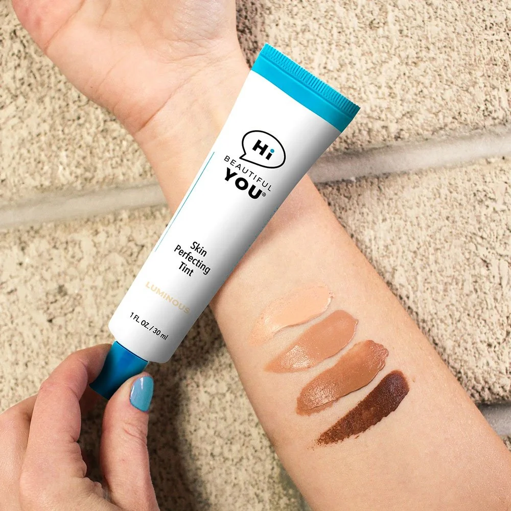 Hand holding Hi Beautiful You Skin Perfecting Tint tube with four shade swatches on forearm showing Luminous Radiant Rich and Decadent