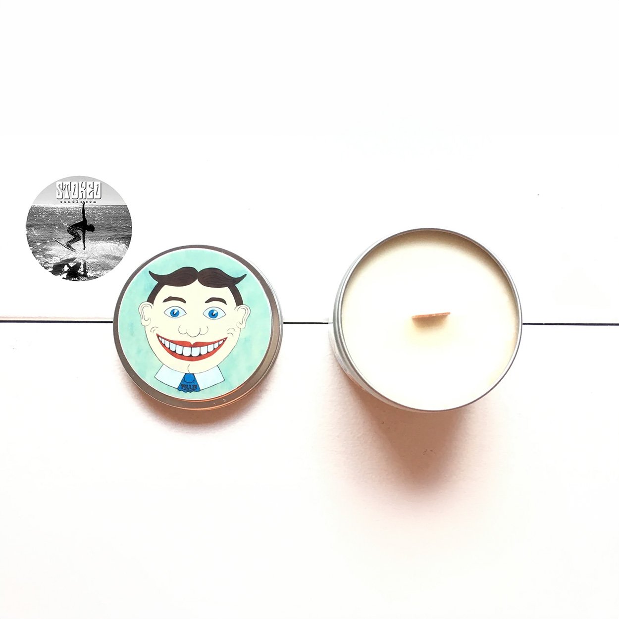 Stoked Candle Tillie Asbury Park tin open alongside Tillie illustrated lid on white background