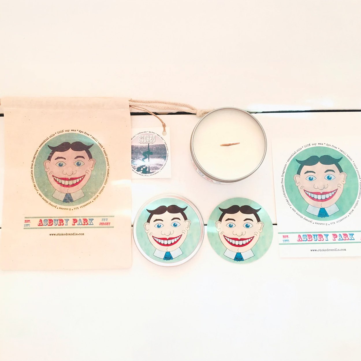 Stoked Candle Tillie Asbury Park gift set flatlay showing tin, Tillie drawstring bag, stickers, and care card on white background