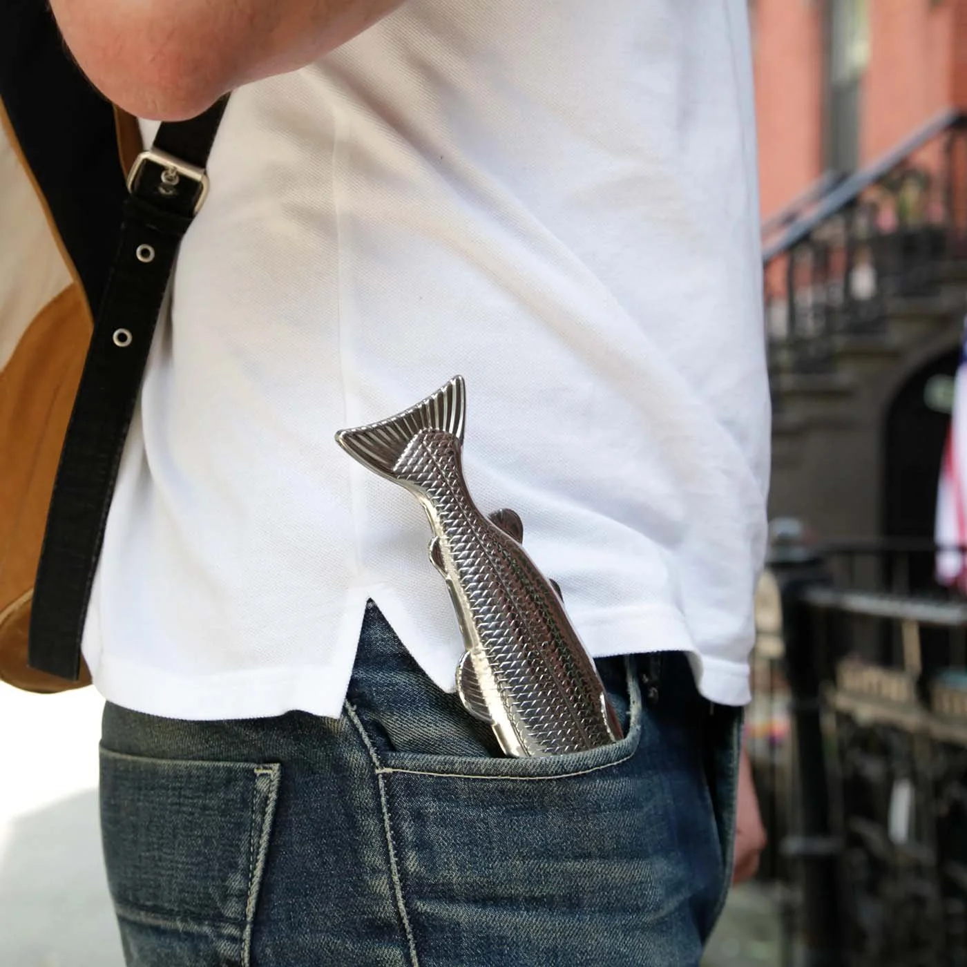 Silver fish flask tucked in the front pocket of jeans on a man wearing a white shirt outdoors