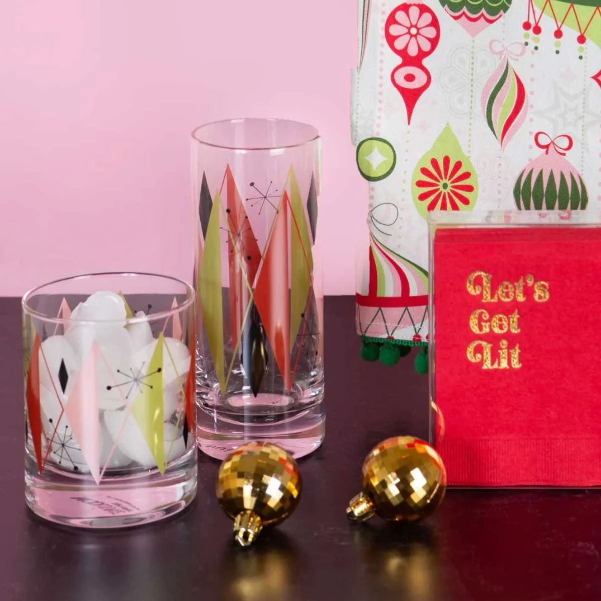 Atomic diamond retro rocks and highball glasses with bold print gift bag and gold disco ball ornaments on dark surface