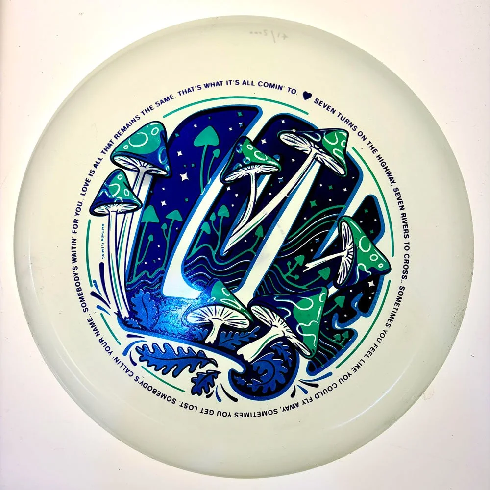 White glow frisbee with deep blue and green mushroom galaxy illustration and lyric text border