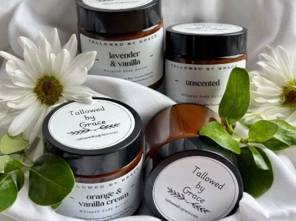 Tallowed by Grace whipped tallow moisturizer jars in multiple scents with white flowers and green leaves on linen background