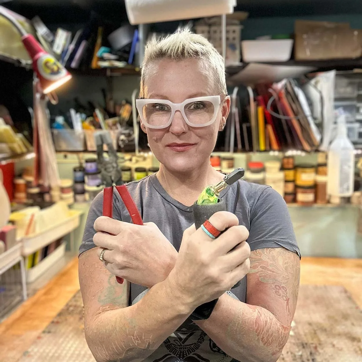 Kiku glass artist Laurie Freivogel holding glass tools in her studio surrounded by art supplies and glass materials