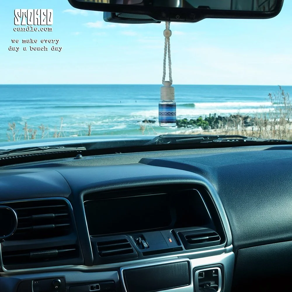 Stoked Freshie scented hanging diffuser hanging from car rearview mirror with ocean and breaking waves visible through windshield