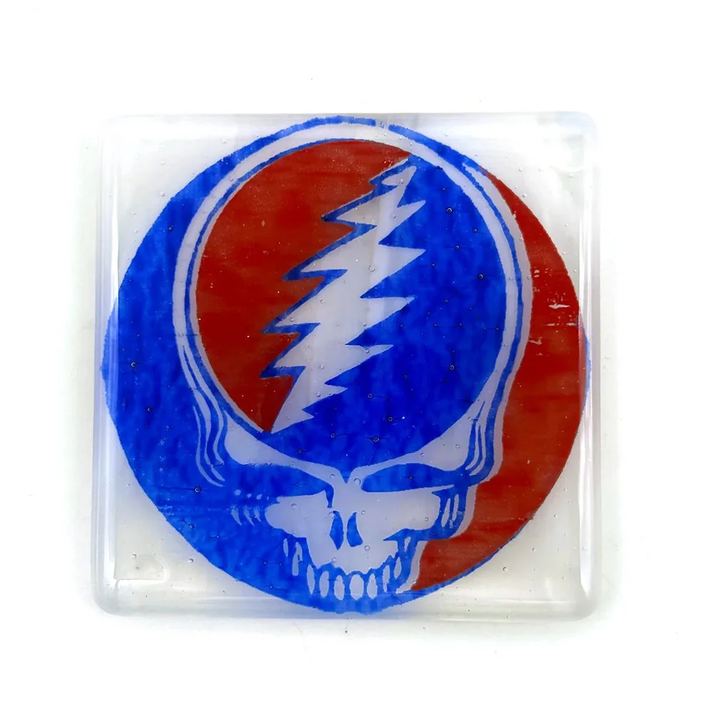 Overhead view of a clear kiln-formed glass coaster with a bold red and blue lightning bolt skull design
