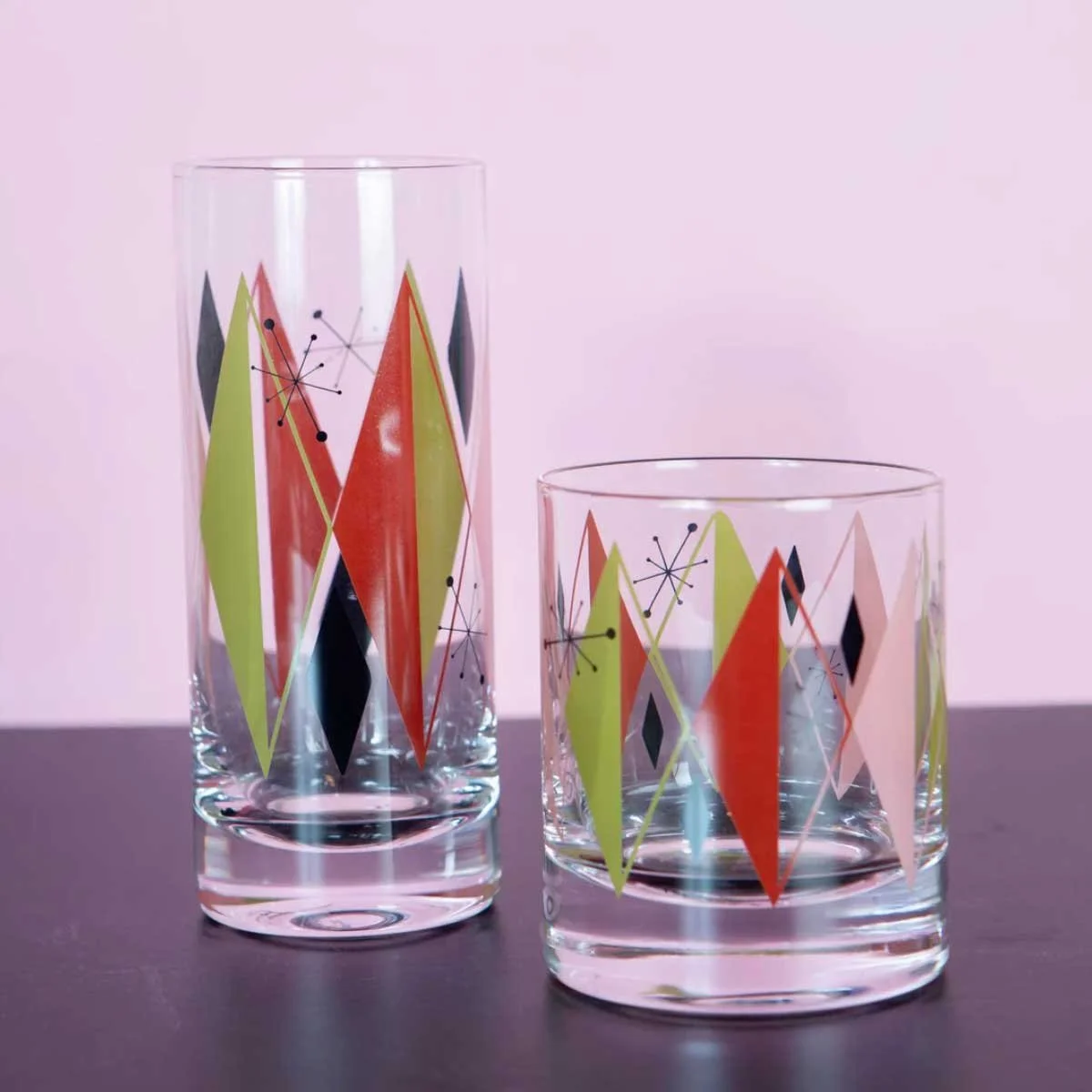 Atomic retro highball and rocks glass set with colorful diamond and starburst pattern on pink background