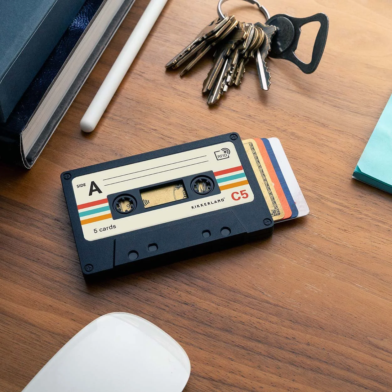 Black cassette tape shaped RFID card holder with credit cards on a wooden desk with keys and mouse