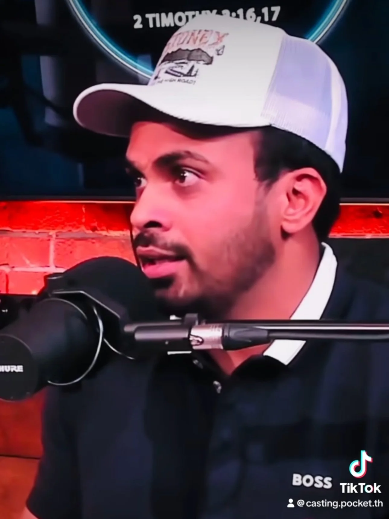 Man wearing a white trucker cap speaking into a microphone during a recording or interview session.