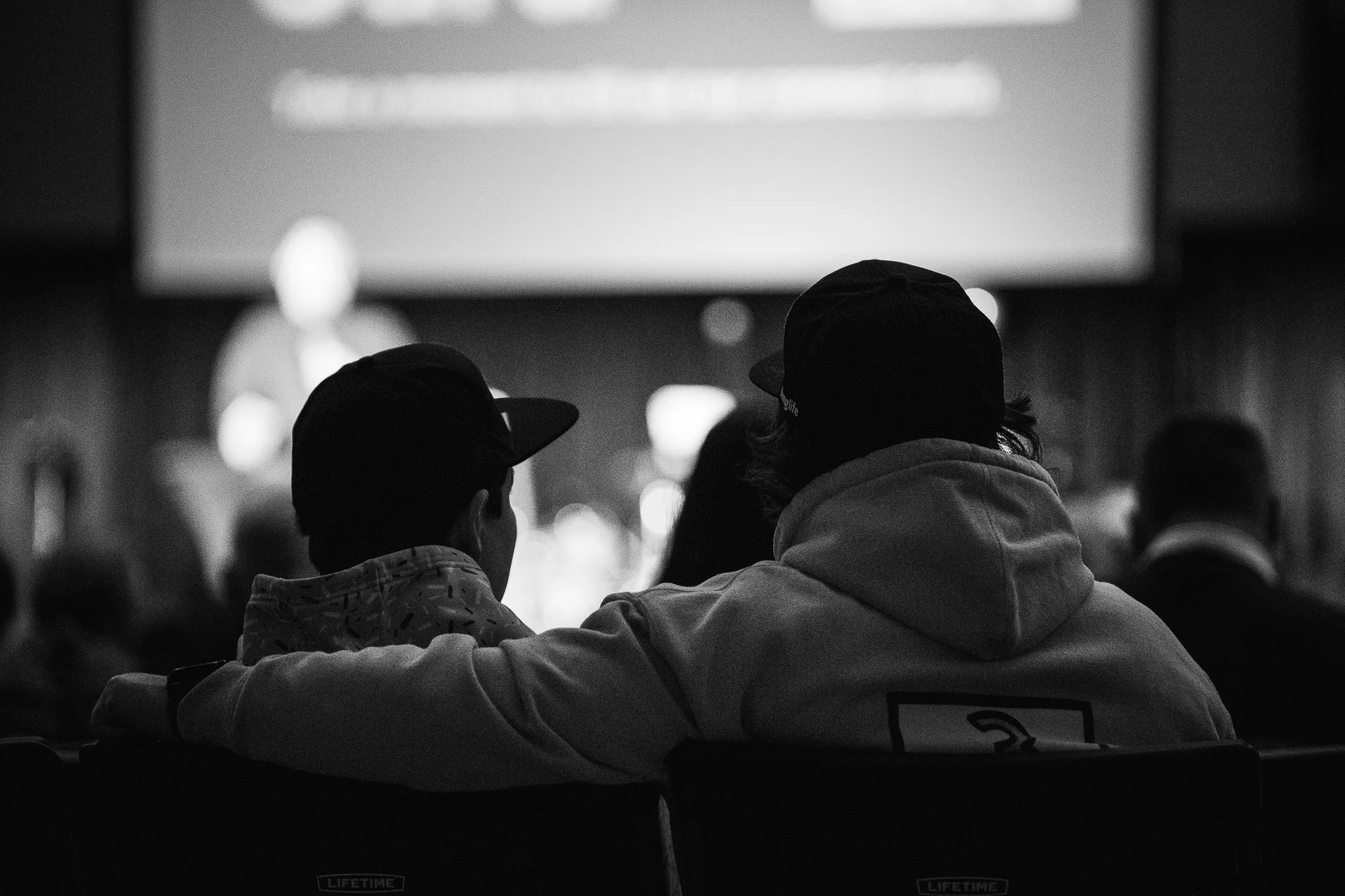 Coffee station with stainless steel coffee dispensers, stacks of white disposable cups, a bottle of syrup, and pumpkin muffins on a black tablecloth.