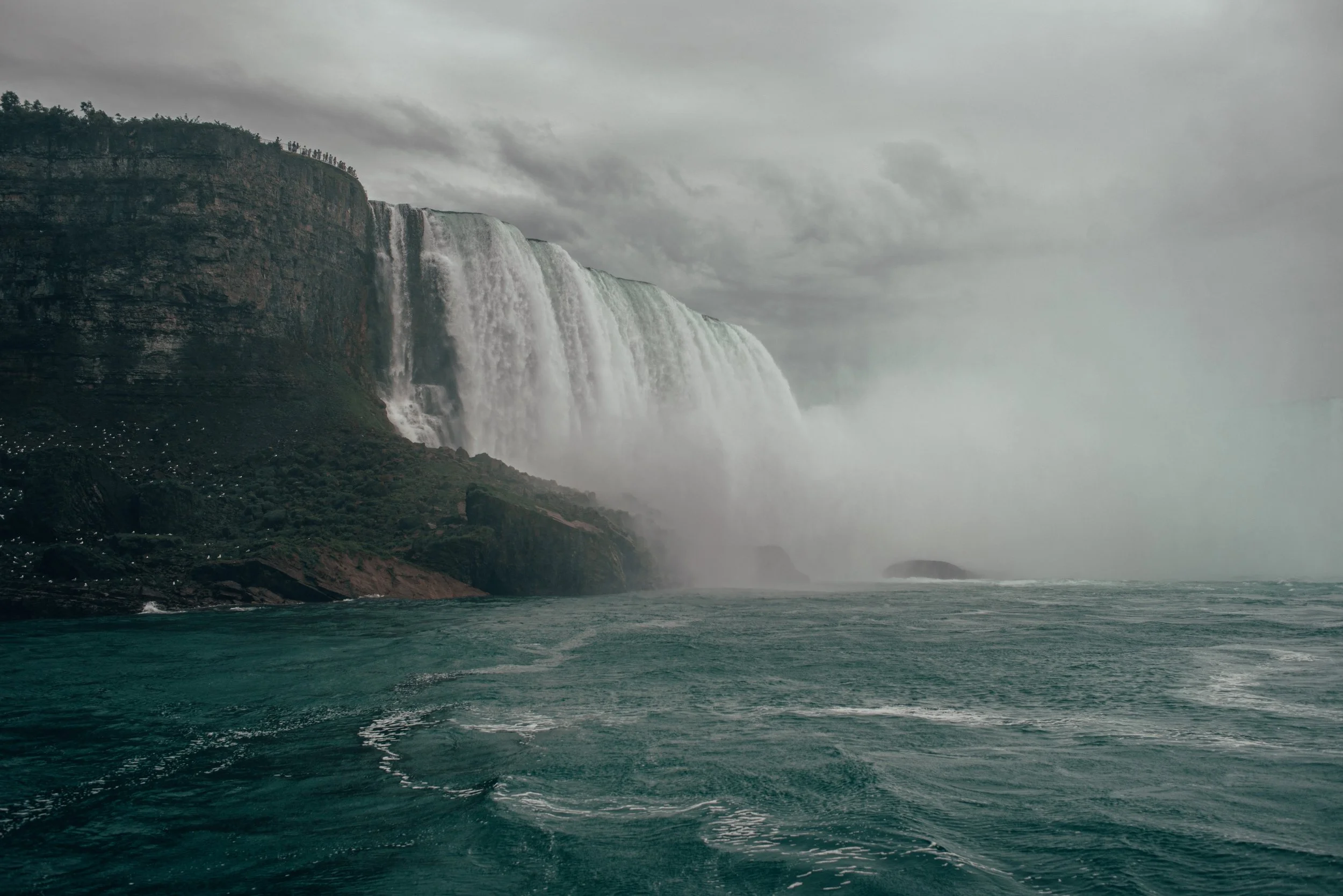 A large waterfall cascading from a cliff into a body of water on a cloudy day.
