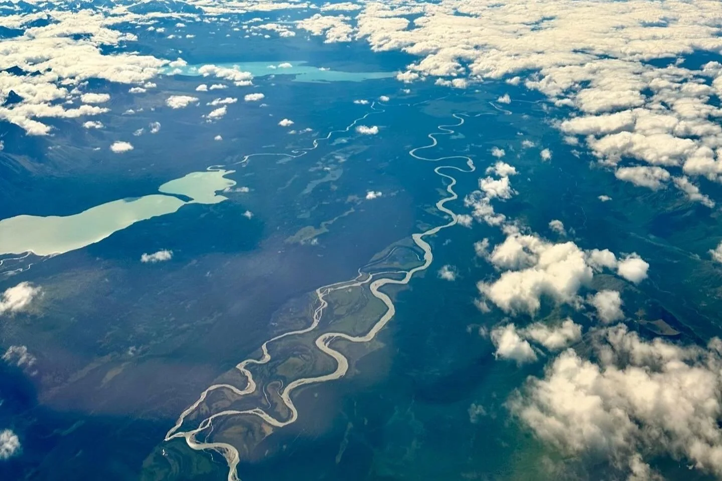 An aerial view of a winding river and lakes, seen through scattered clouds.