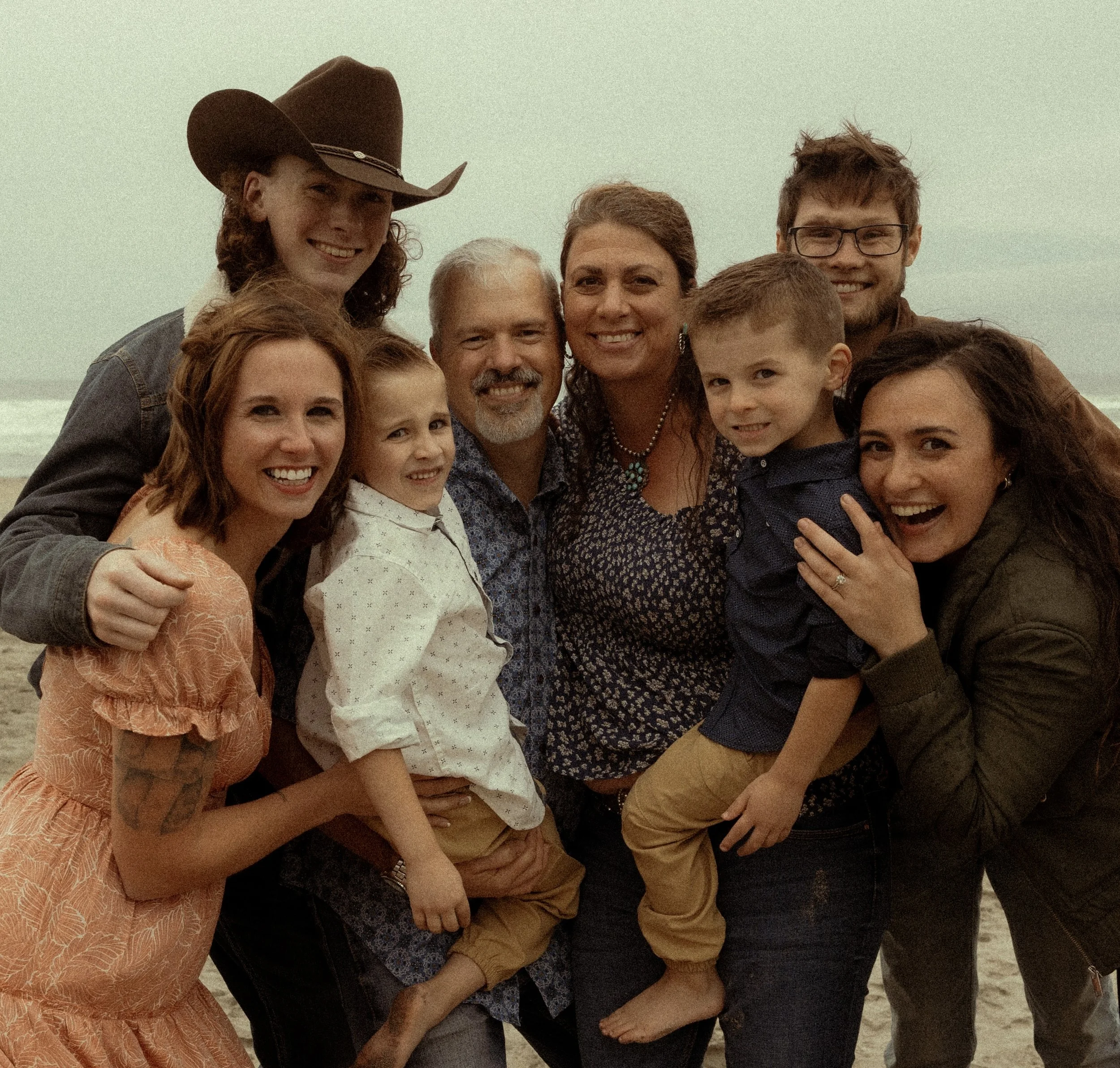 A large family of nine people gathered on the beach, smiling for the camera.
