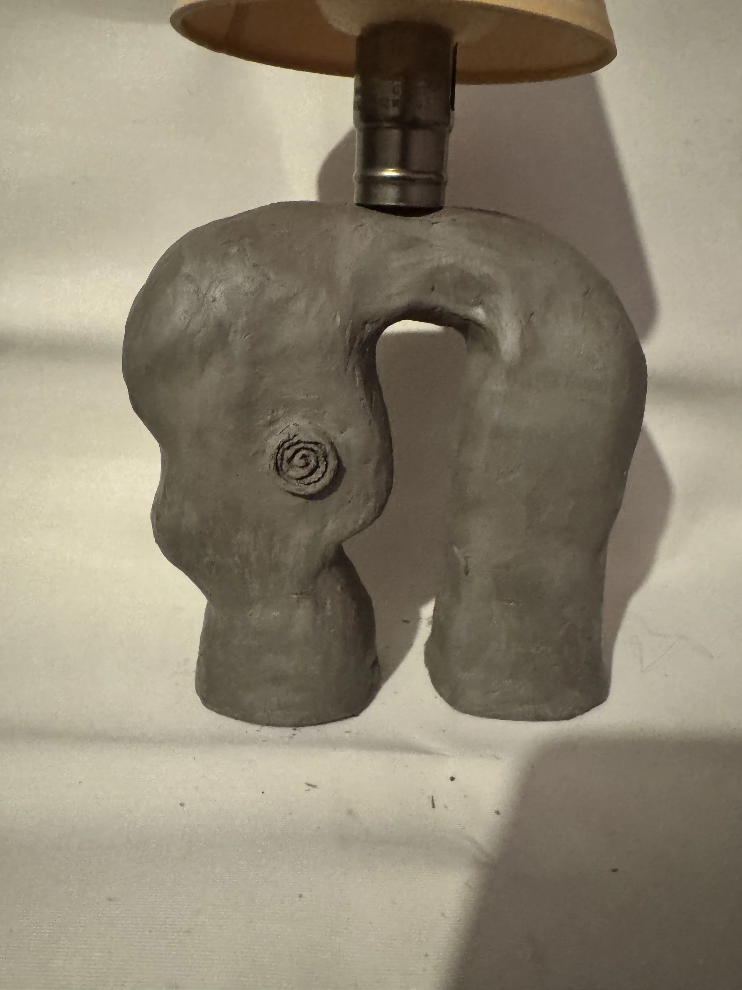 A lamp with a base designed to resemble a small, abstract elephant head with trunk, ears, and a visible eye, made of a gray material, possibly concrete or stone.
