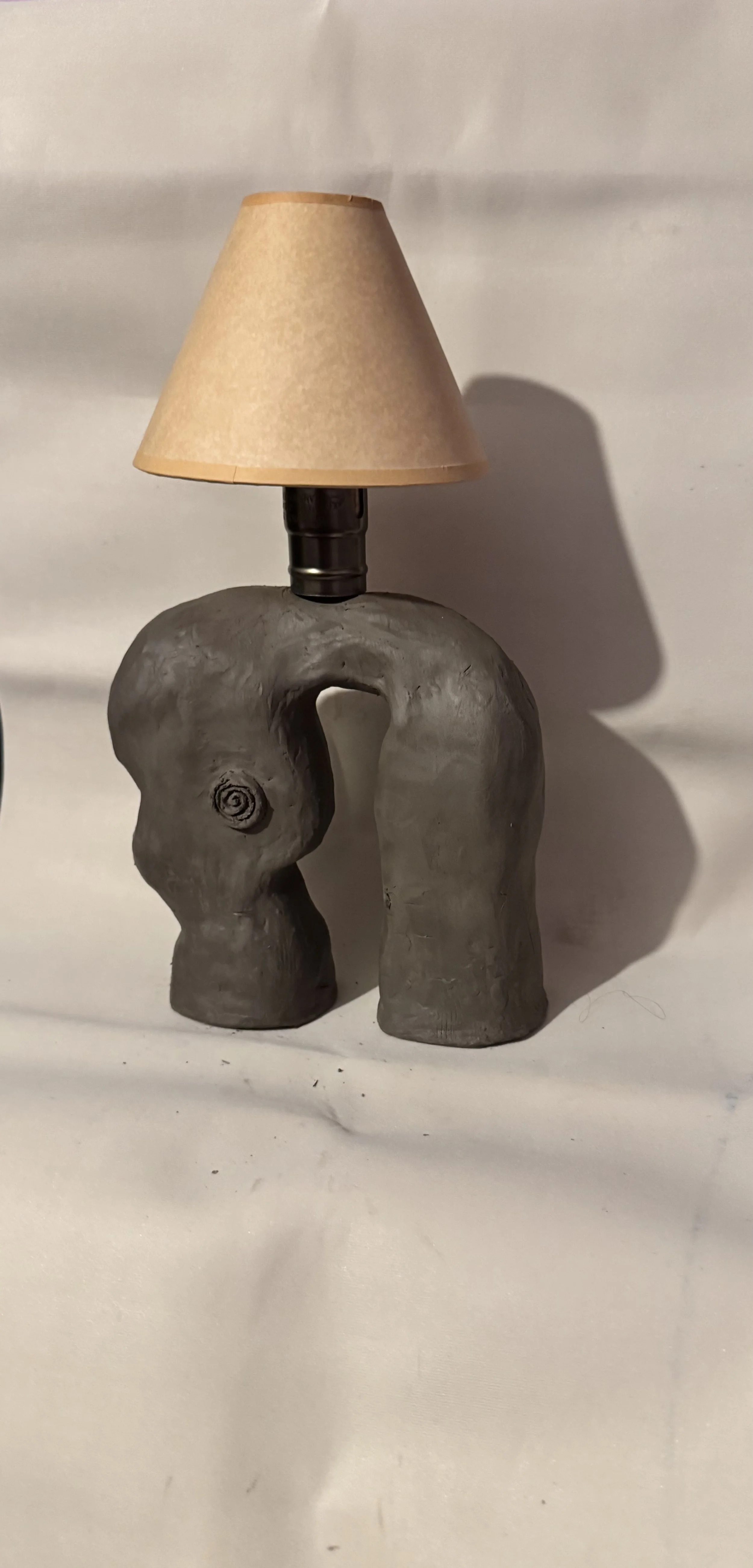 A table lamp with a base shaped like an abstract gray elephant and a beige lampshade.