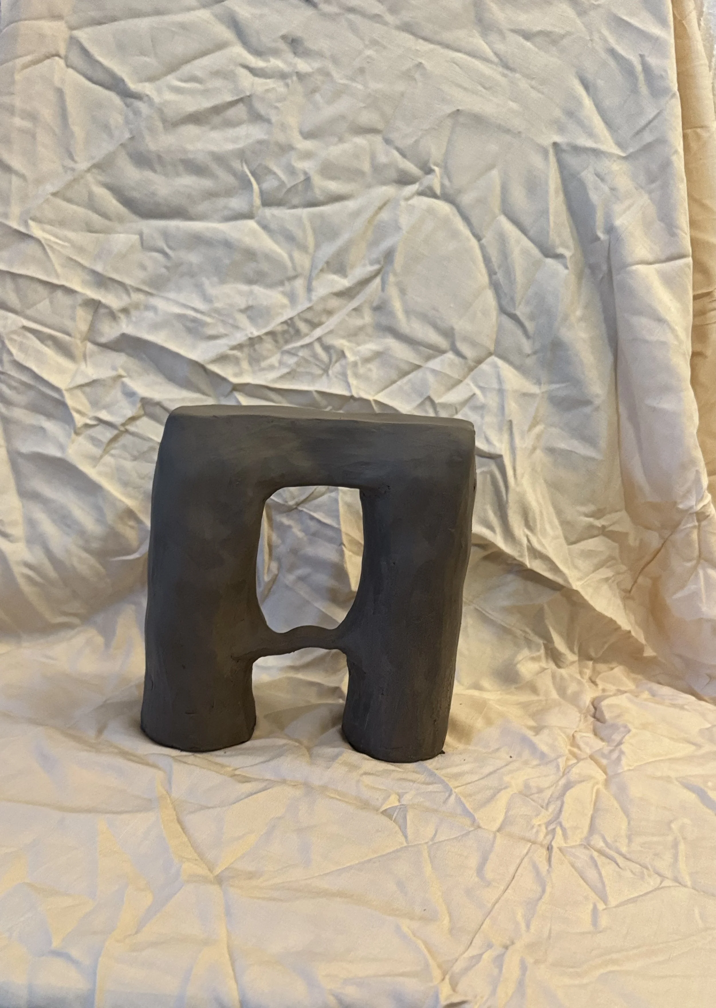 A small, black, abstract sculpture with a square hole in the center, placed on crumpled white paper.