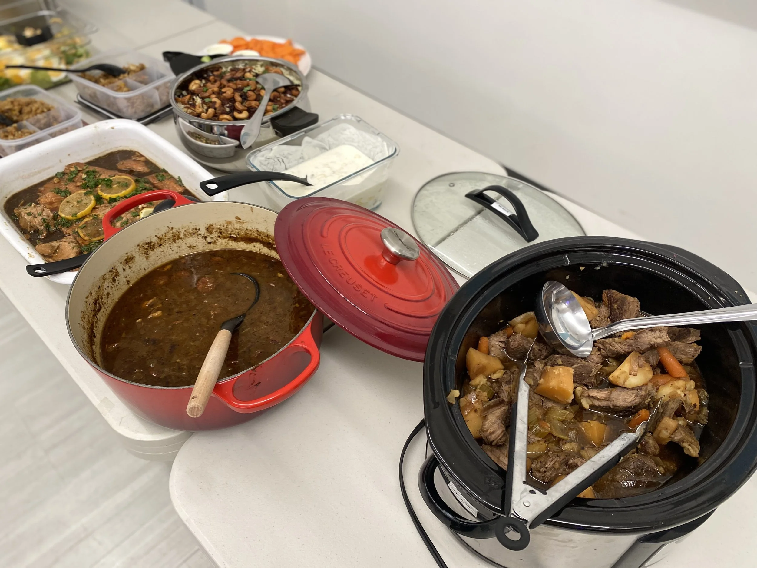 Table with various slow-cooked dishes, including beef stew and pot roast, along with side dishes, condiments, and toppings.