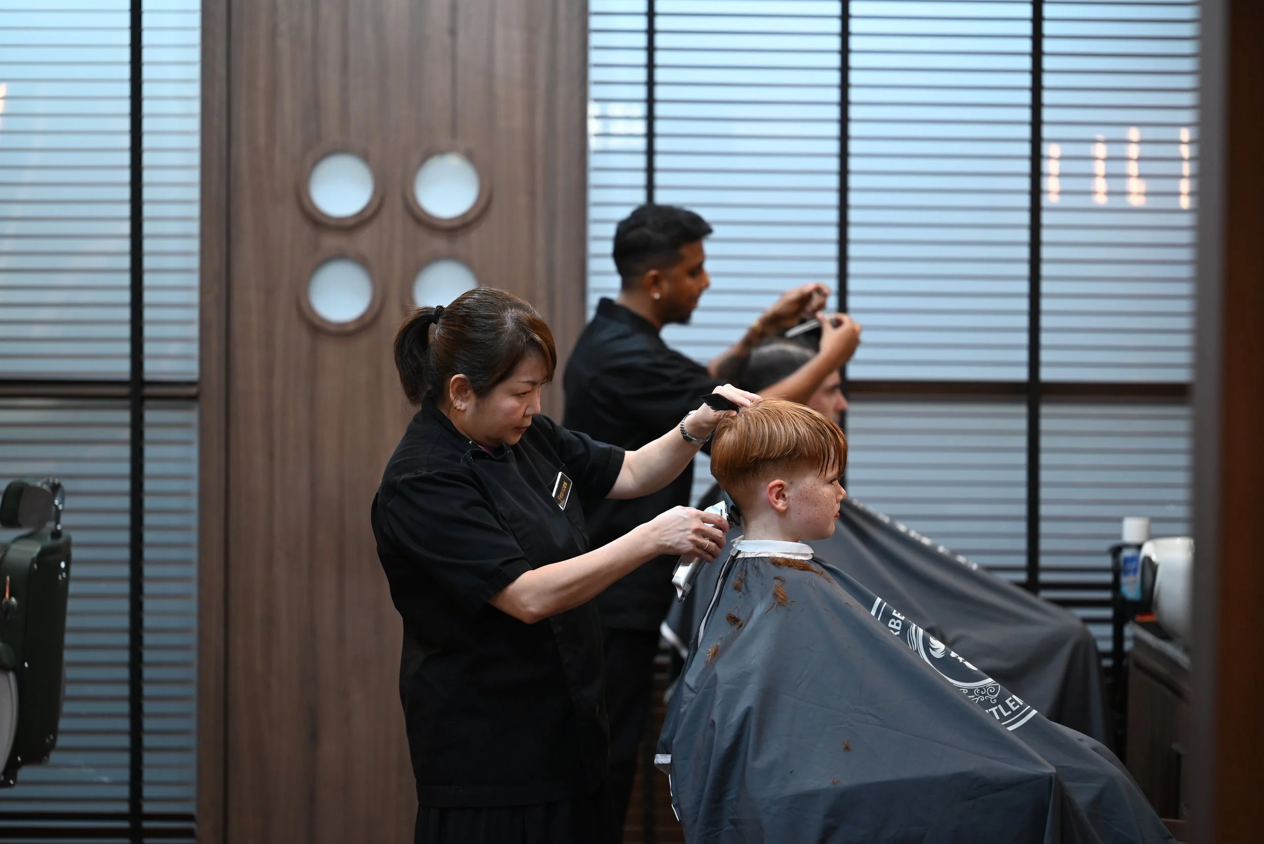 Double trouble in the barber’s chair — dad’s getting sharp, and junior’s learning early that greatness starts with a fresh cut.