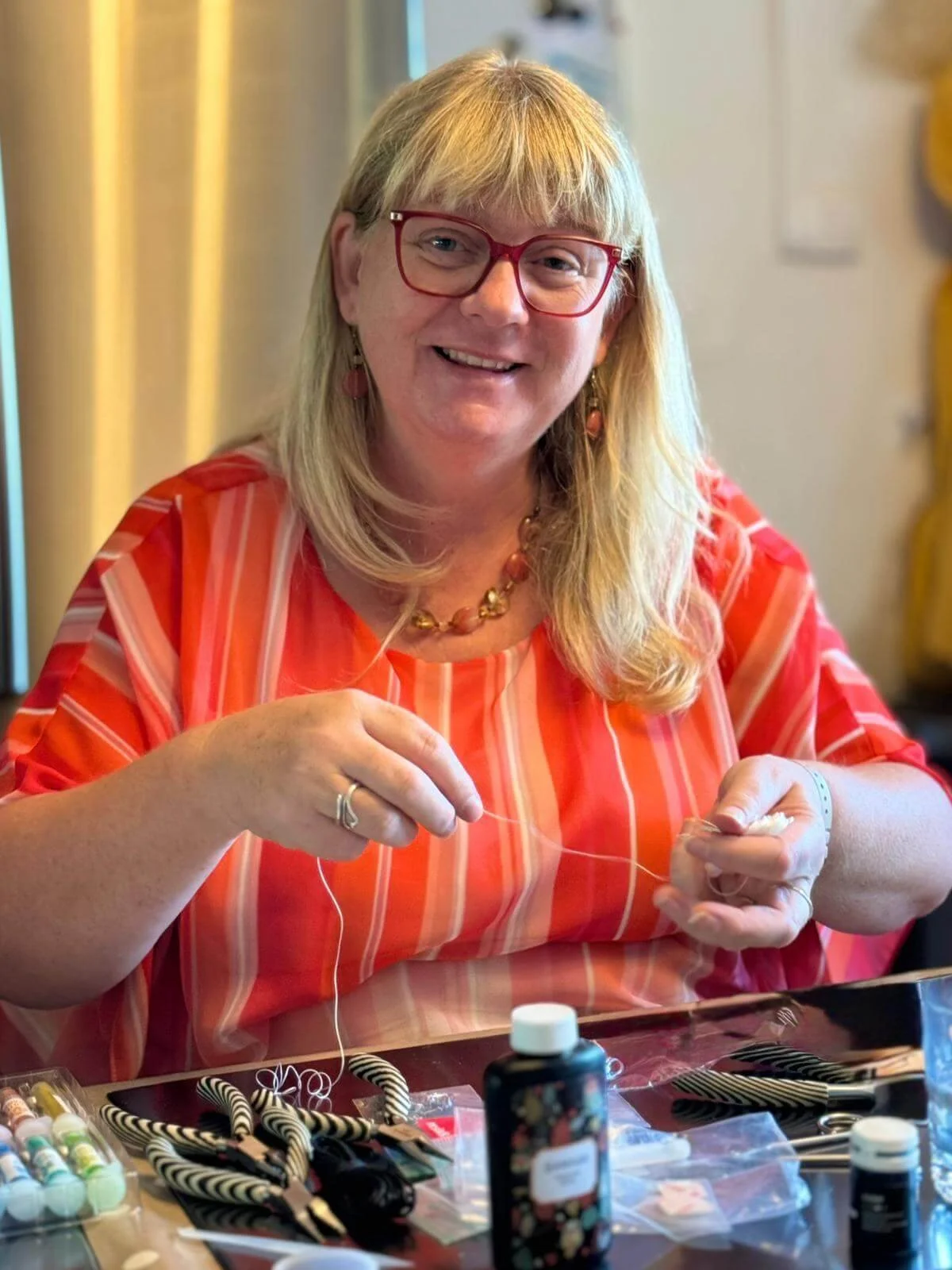 Katherine smiling in a stripy orange top making jewellery
