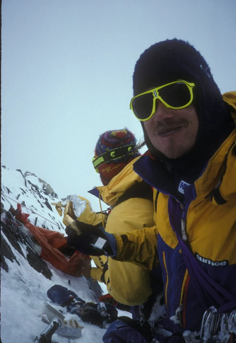 July 1988: Kevin Doyle enjoying a four year-old Cadbury Fruit & Nut bar recovered from a tattered haul bag we found “clipped to a piton at 22,000 feet. Barry cut it open without expectation. 60 pitons spilled out, followed by a dozen ice screws, choc