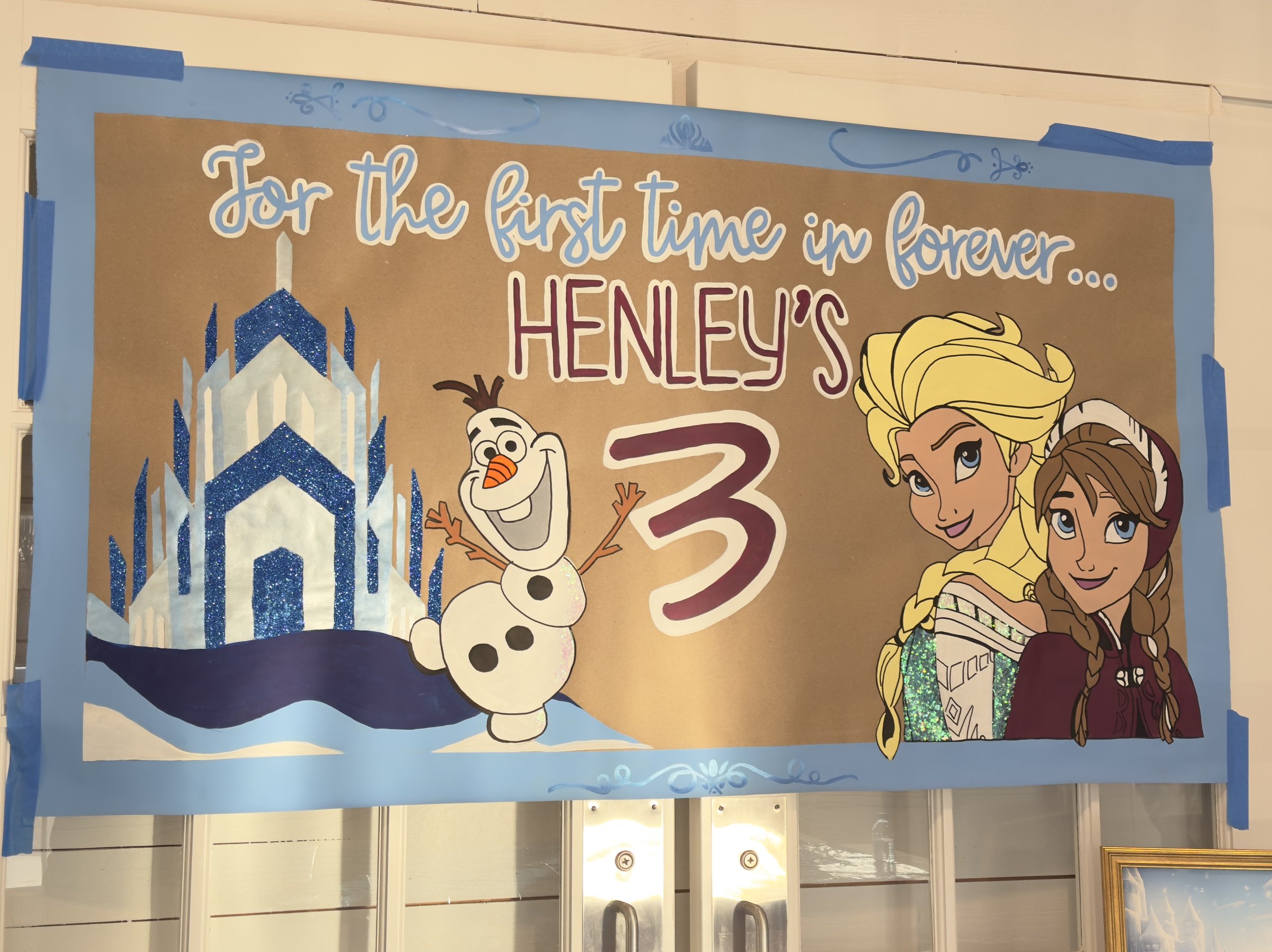Birthday banner with Frozen theme, featuring a snowman, an ice castle, and two princess characters, celebrating Henley's third birthday.