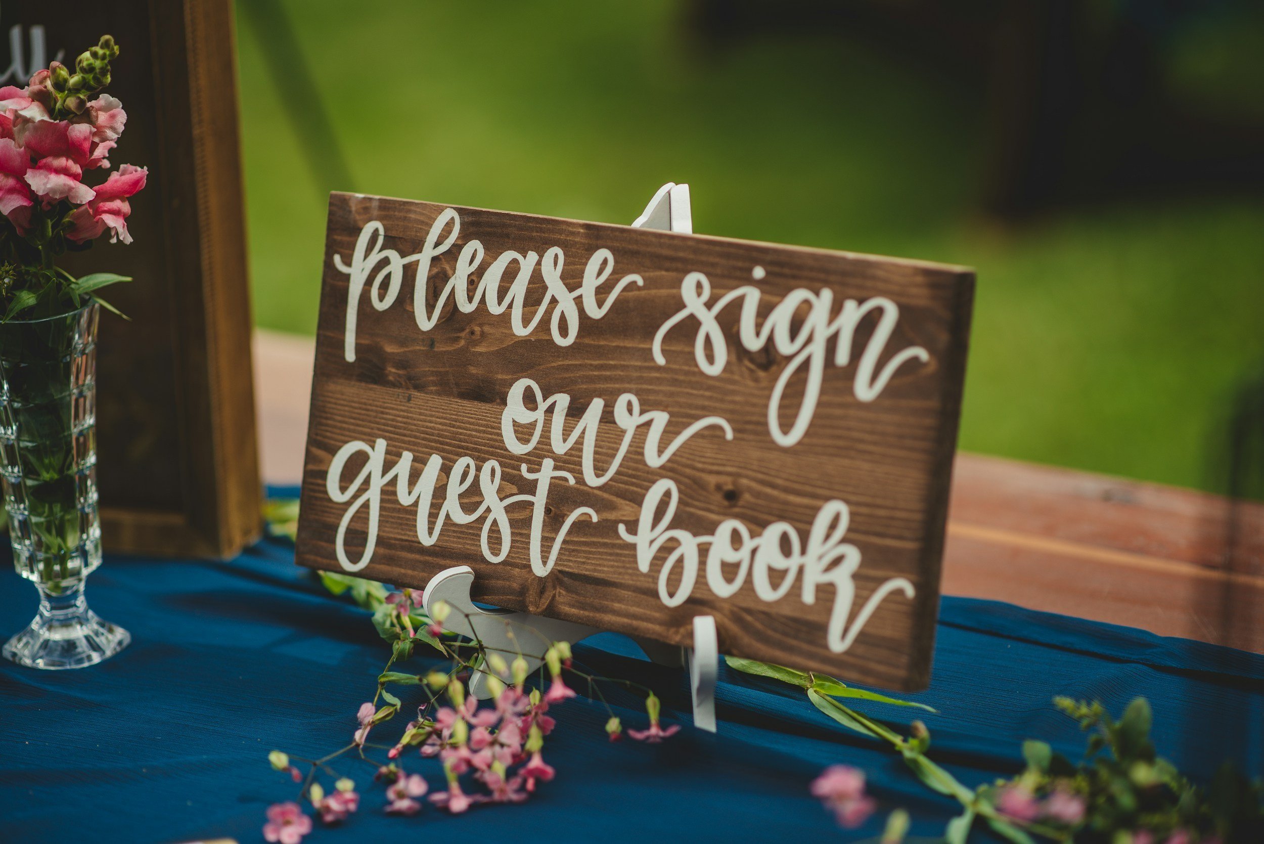 Event-specific canvas sign reading 'please sign our guest book' displayed at an outdoor event.