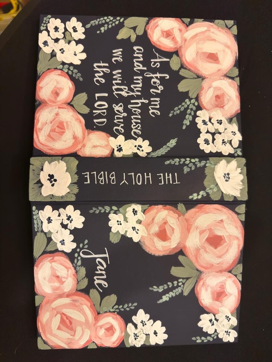 Top-down view of a custom-painted Bible, showcasing floral designs on the spine and cover.