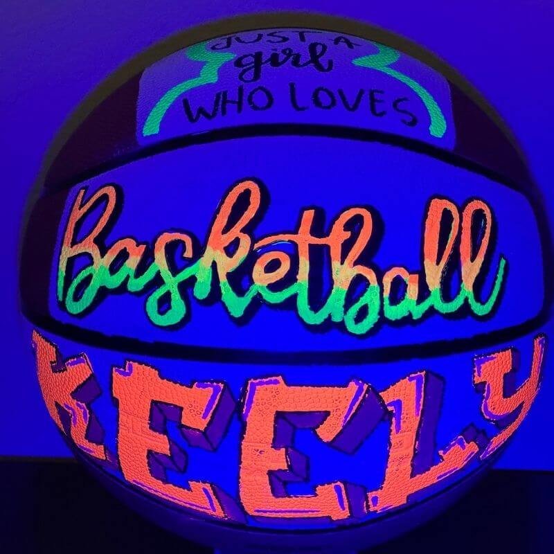 Glowing basketball under blacklight with phrases "Just a girl who loves Basketball" and the name "Keely" in bright, vibrant colors.
