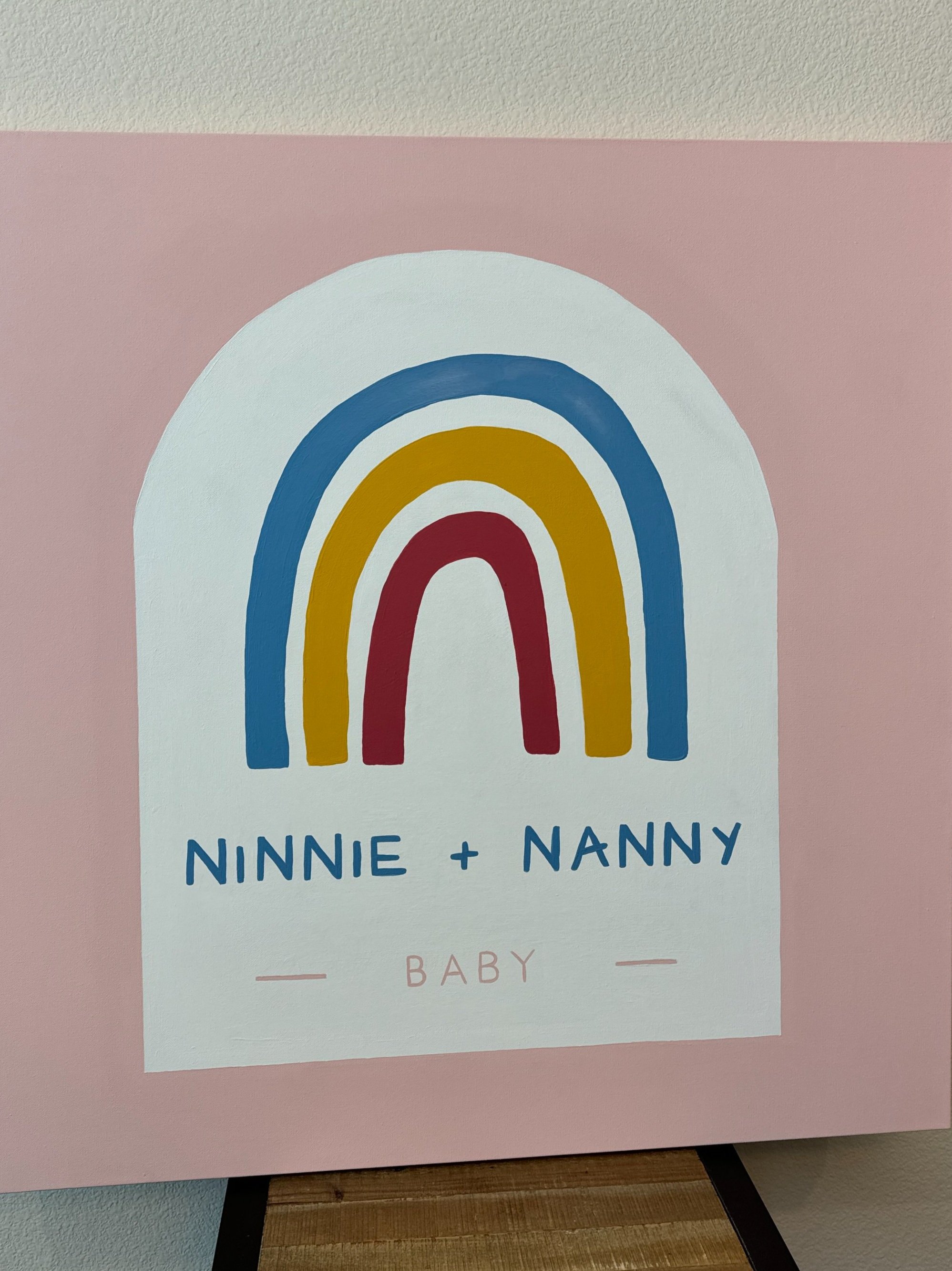 Custom baby canvas with a rainbow design and the text 'Ninnie + Nanny Baby.'