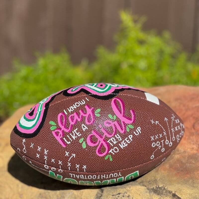Colorful American football with text "I know I play like a girl, try to keep up," featuring decorative designs and play diagrams.