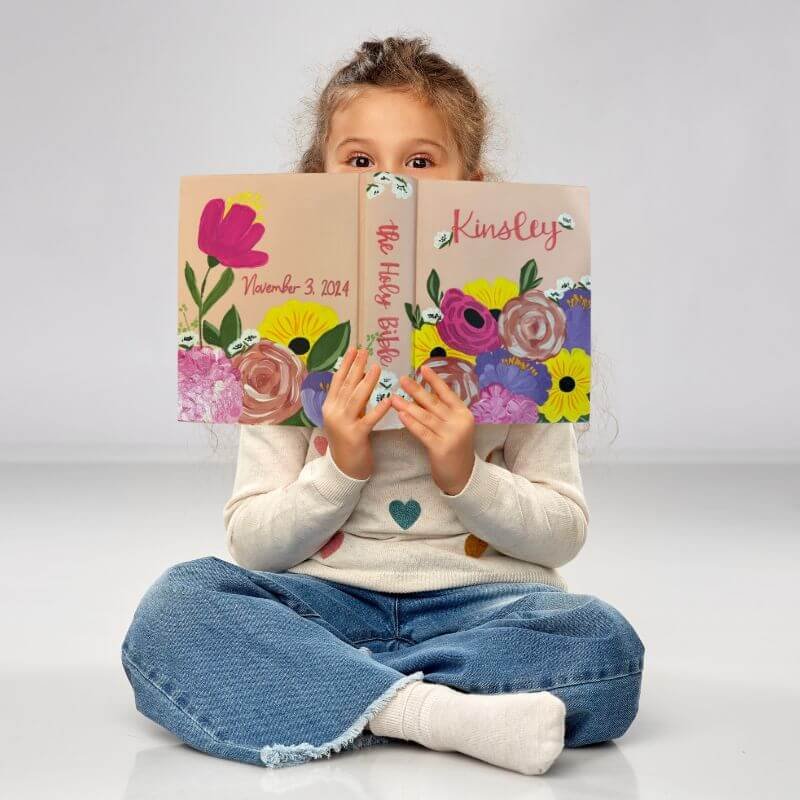 Young girl holding personalized bible with pink florals and "Kinsley" painted on the cover.