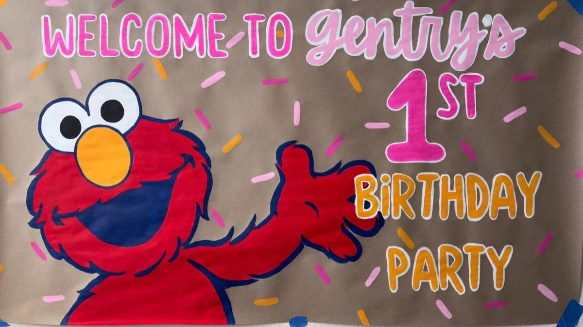 Hand-painted custom banner featuring Elmo with colorful sprinkles and text that reads, "Welcome to Gentry’s 1st Birthday Party."