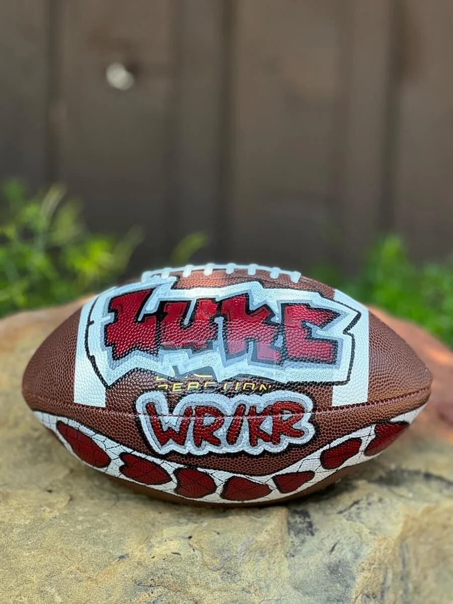 Custom football with graffiti-style writing in red and white saying "Luke."