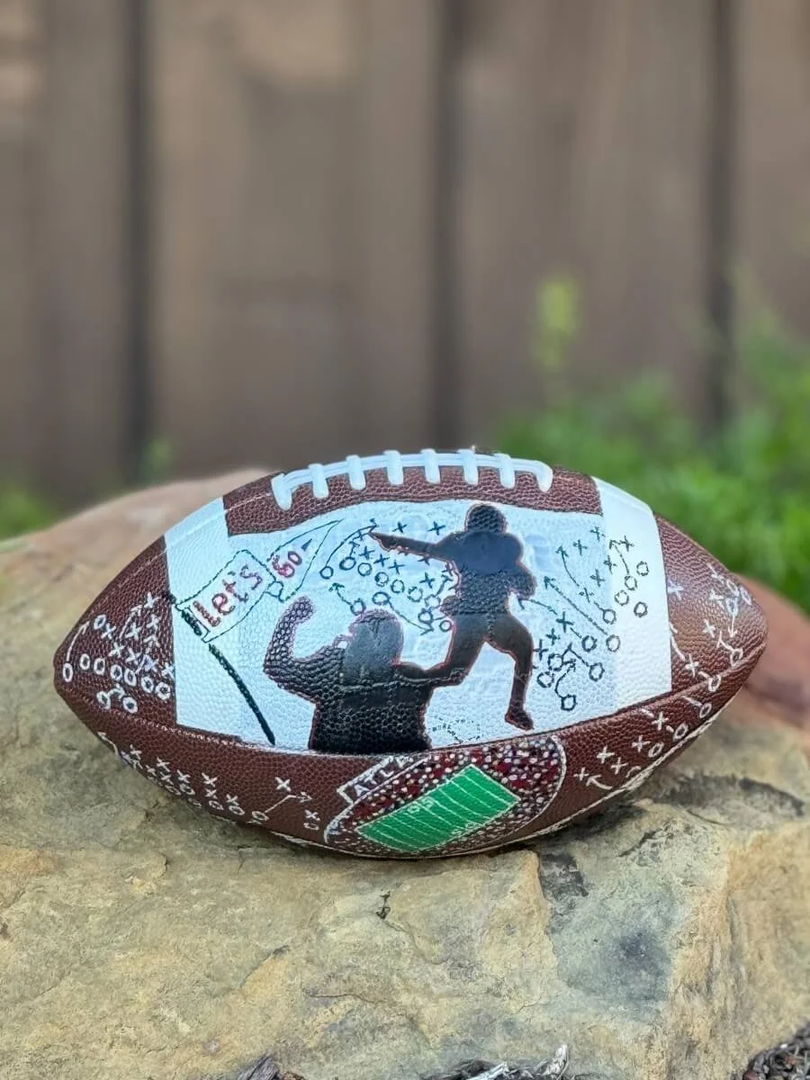 Custom football featuring a player in black silhouette, resting on a rocky surface.