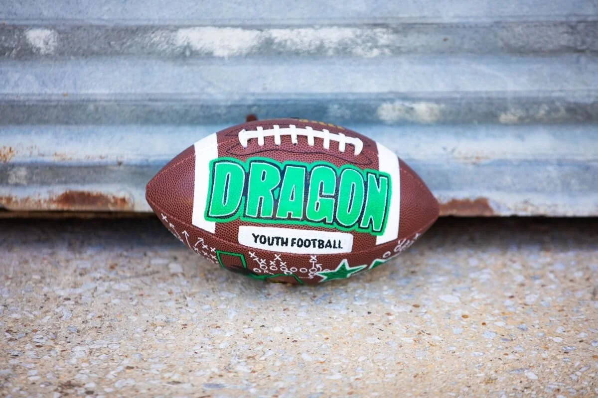 Customized football with "Dragon Youth Football" lettering, resting on concrete.