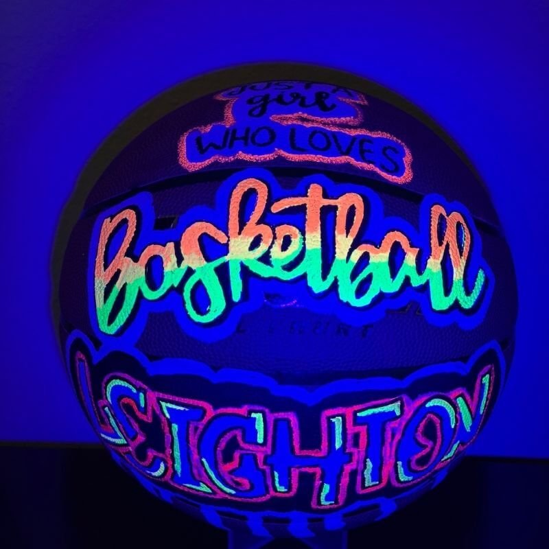 Blacklight-illuminated basketball with neon text "Just a girl who loves basketball" and "Leighton."