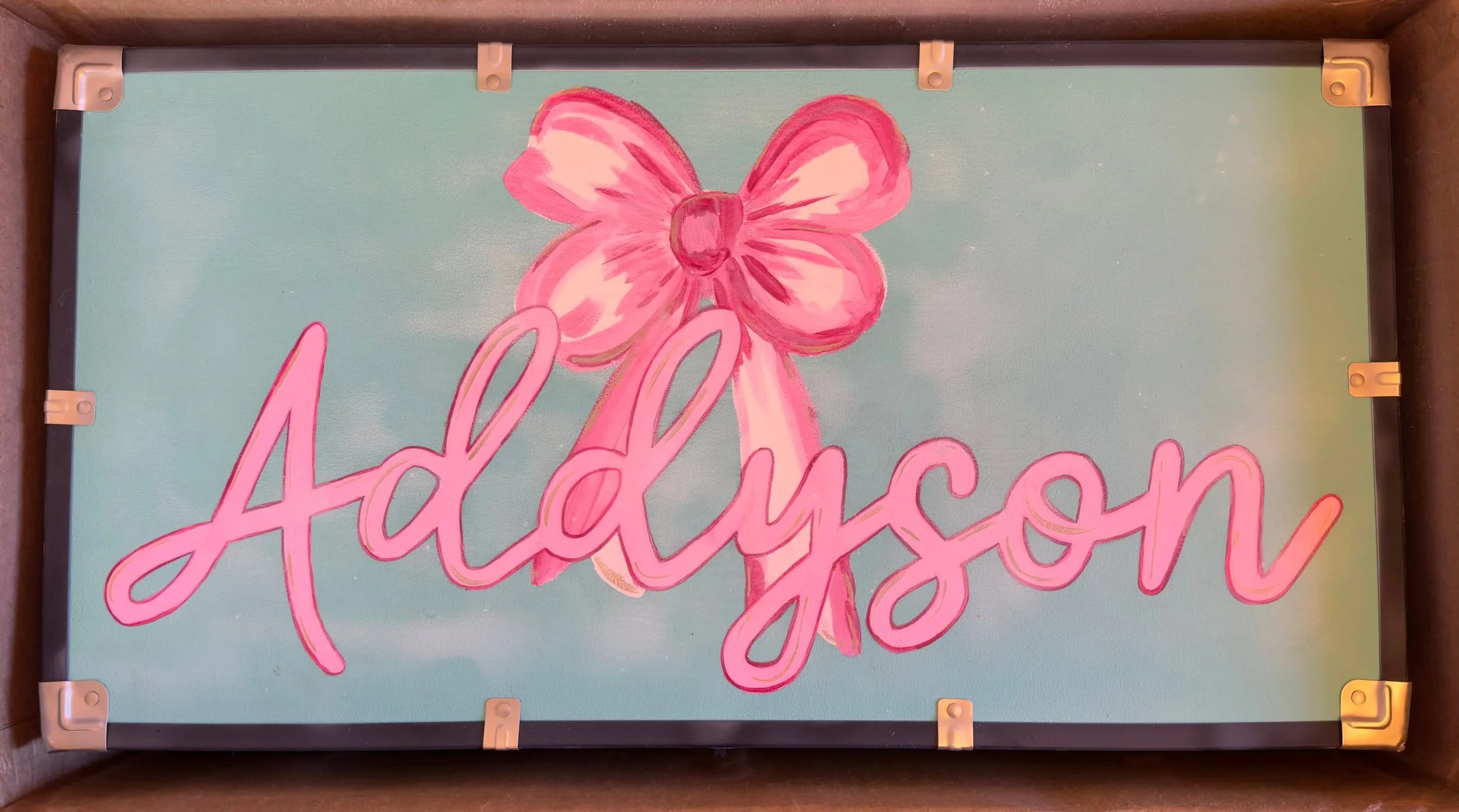 Sign with the name 'Addyson' written in pink script, featuring a pink bow drawn above the name, on a light blue background.